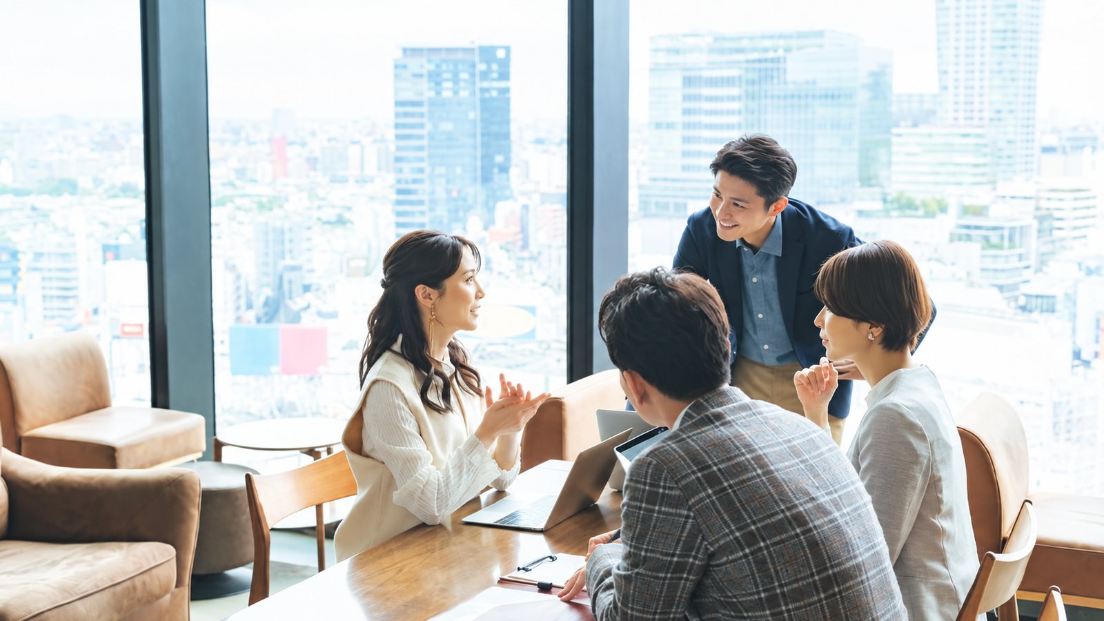街を見下ろす窓際の会議スペースで打ち合わせをする4人の会社員